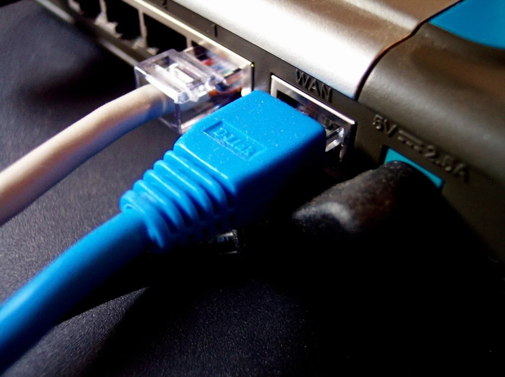 A close up of a blue ethernet cable connected to a laptop. Computer internet cable, computer communication